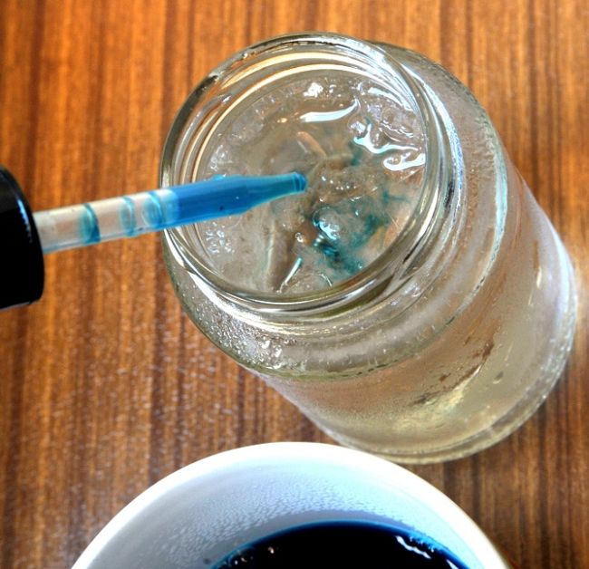 Water dropper adding blue water to a jar of clear water with ice