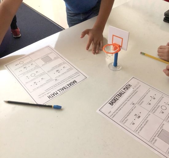 Desktop with a tiny basketball hoop, fraction worksheets, a pencil and a student's hand