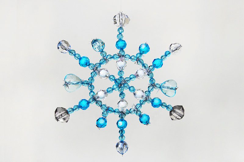 A snowflake is shown that has been created using pipe cleaners and different blue and clear beads.