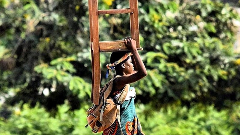 Student carrying chair on head walking outside with trees