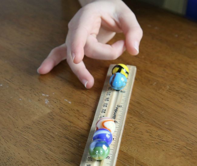 Fourth grade science student flicking a marble along the ridge in a ruler