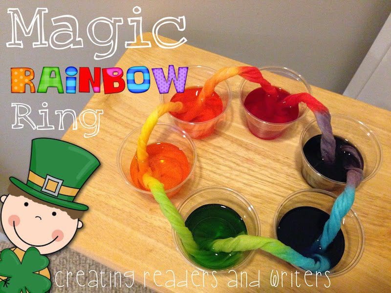 rolled up piece of fabric is dipped into plastic cups filled with water and food coloring on a desk, as an example of St. Patrick's Day activities 