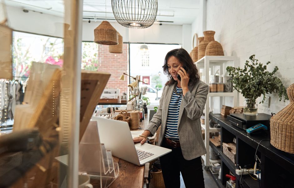 retailers in shop on phone using laptop