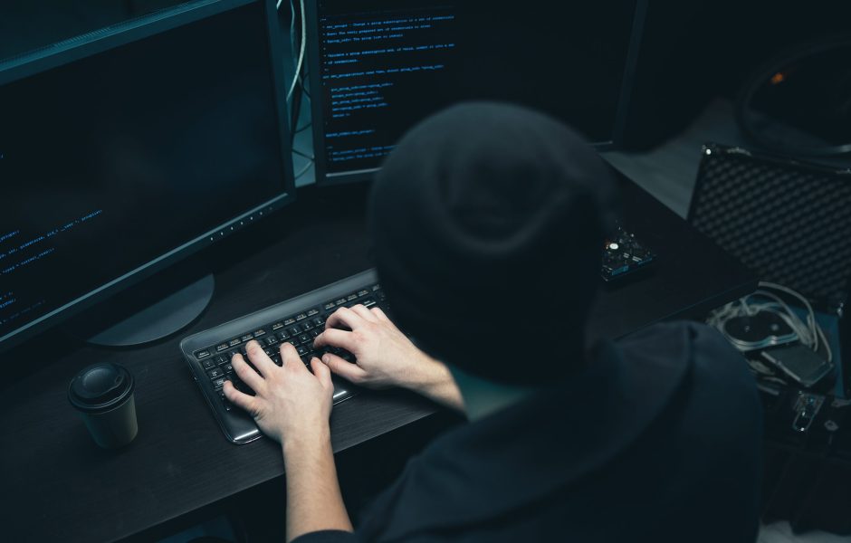 hacker in dark clothing running a triangulation fraud scheme on a computer