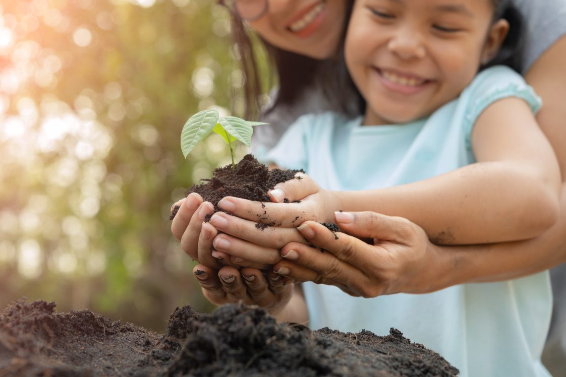 mother and child holding seedling planted in dirt