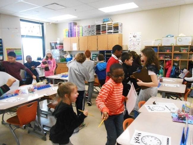 Students dancing around the classroom to look at paper clocks on each other's desks
