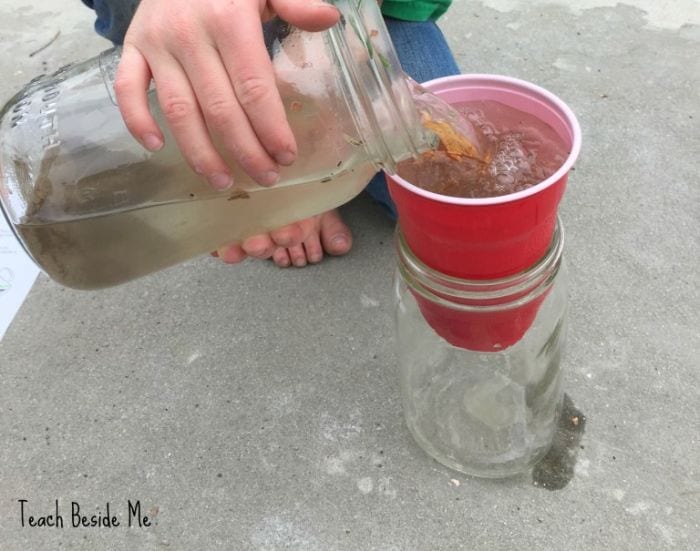 Science student pouring dirty water through a plastic cup into a jar below