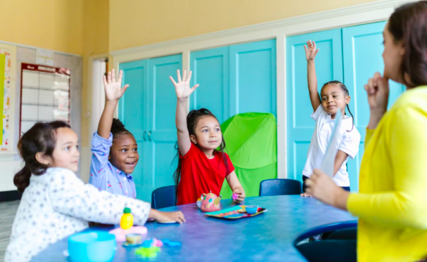 A small group of students play a math game at a table with their teacher 