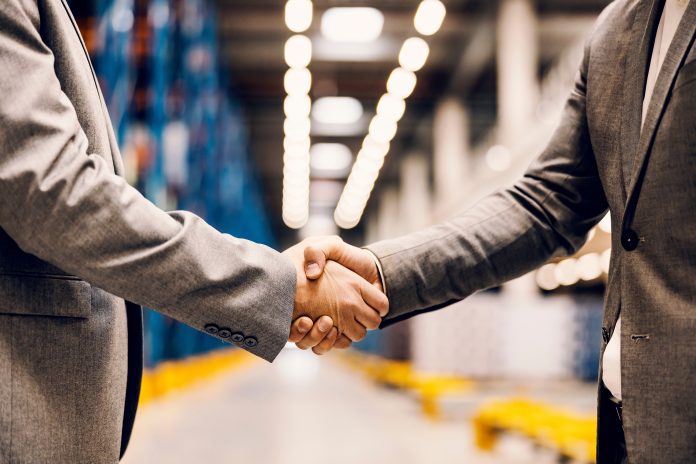 two businessmen shaking hands inside a fulfillment center