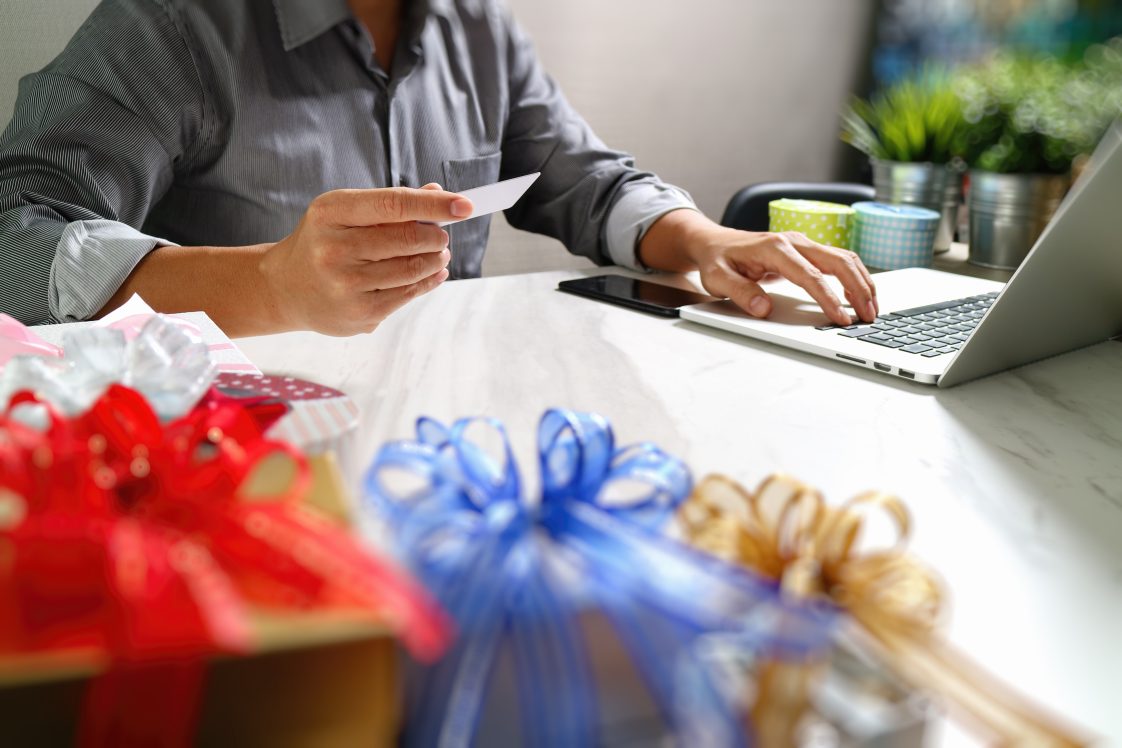 person holding credit card surrounded by gift wrap shopping for the holidays