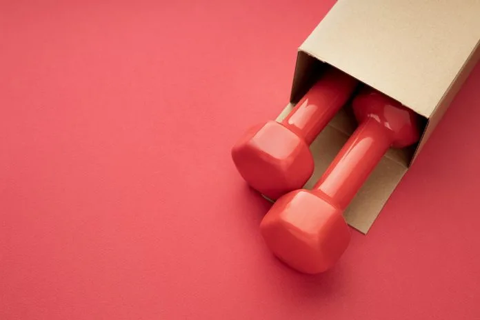 two red dumbbells are visible from a paper box on a red background. package with dumbbells